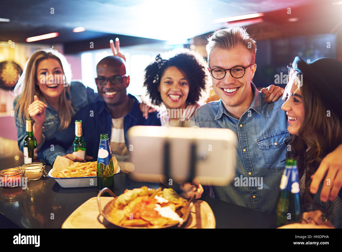 Horizontal indoors shot of cheerful smiling people in the bar making a shot with a selfie-stick. Stock Photo