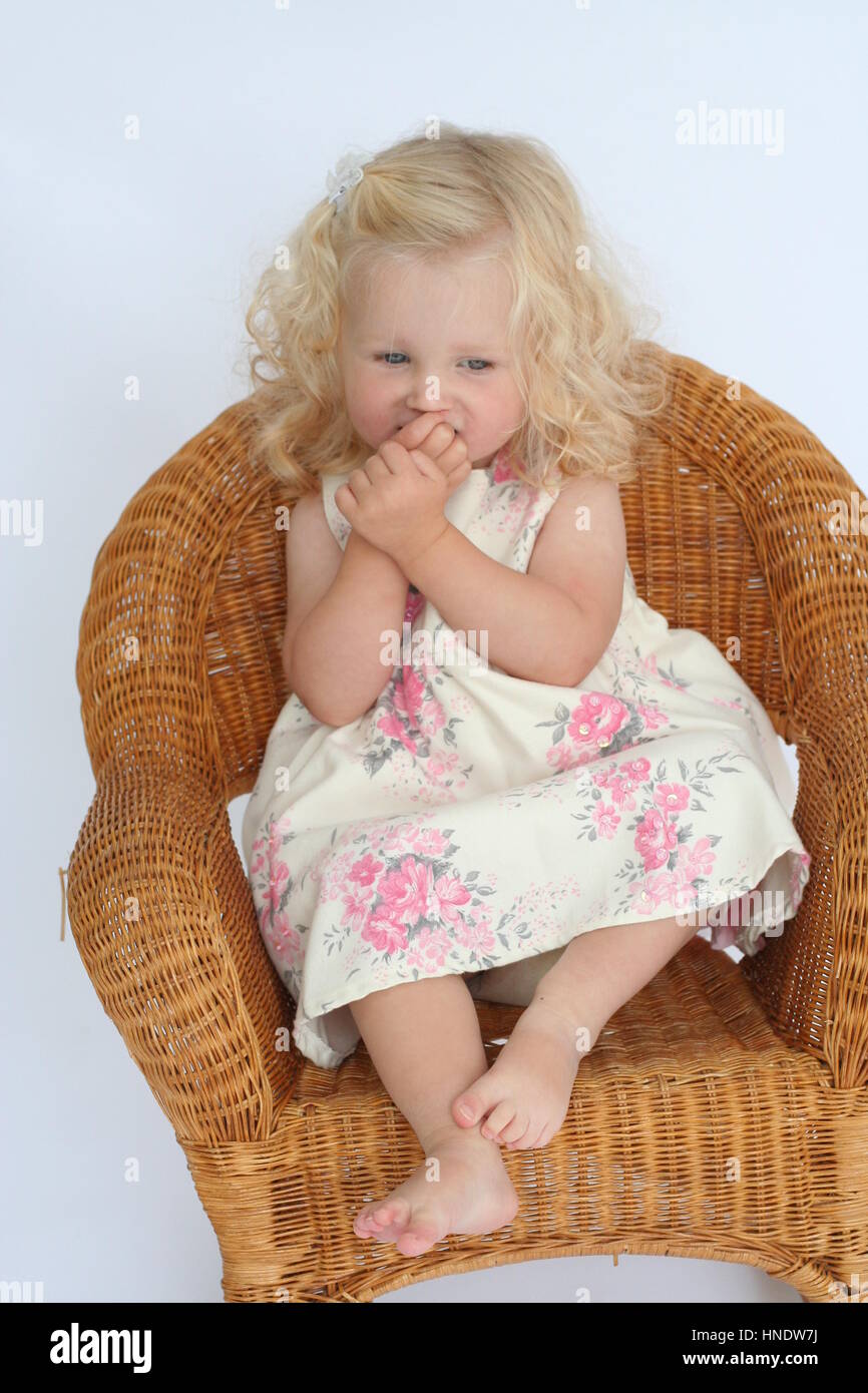 Little Curly Blonde Toddler Girl Sitting In A Wicker Chair Stock