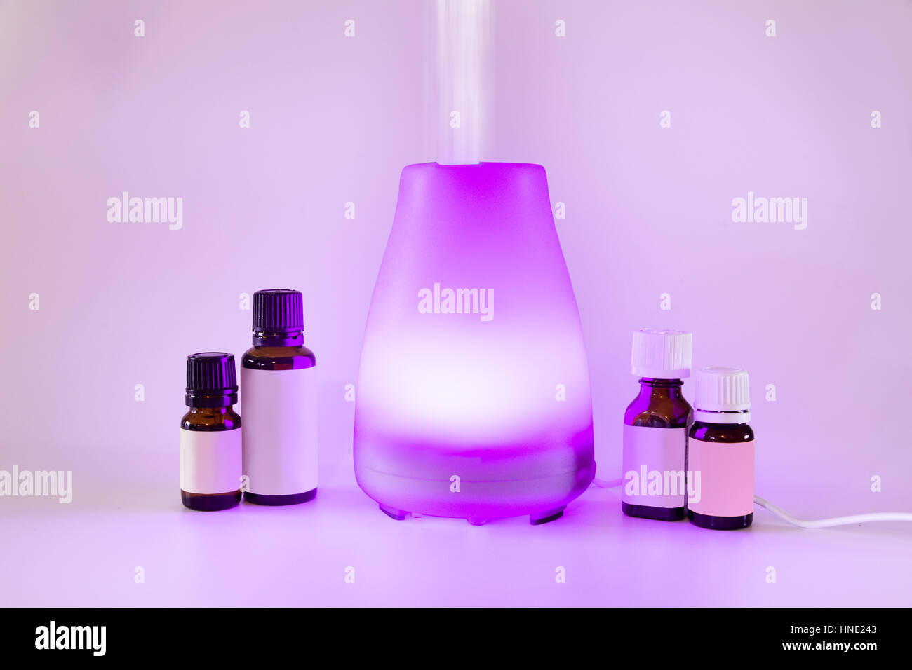 Colorful lit essential oil diffuser with mist and bottles of oils Stock Photo