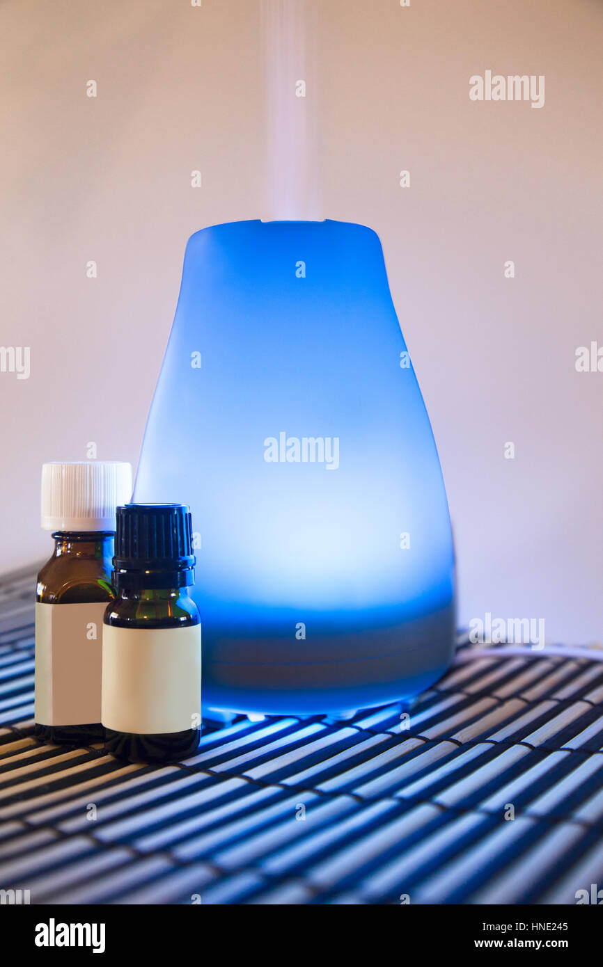 Colorful lit essential oil diffuser with mist and bottles of oils Stock Photo