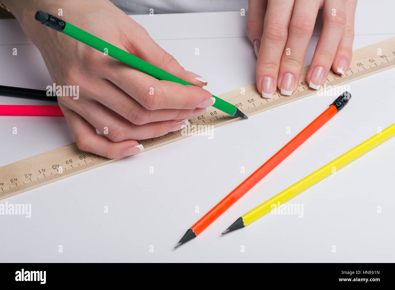 Female hands with classical French manicure draw a pencil by means of a ruler on clean standard sheet Stock Photo