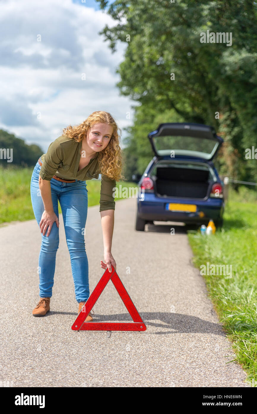 European teenage girl placing hazard warning triangle on rural road Stock Photo