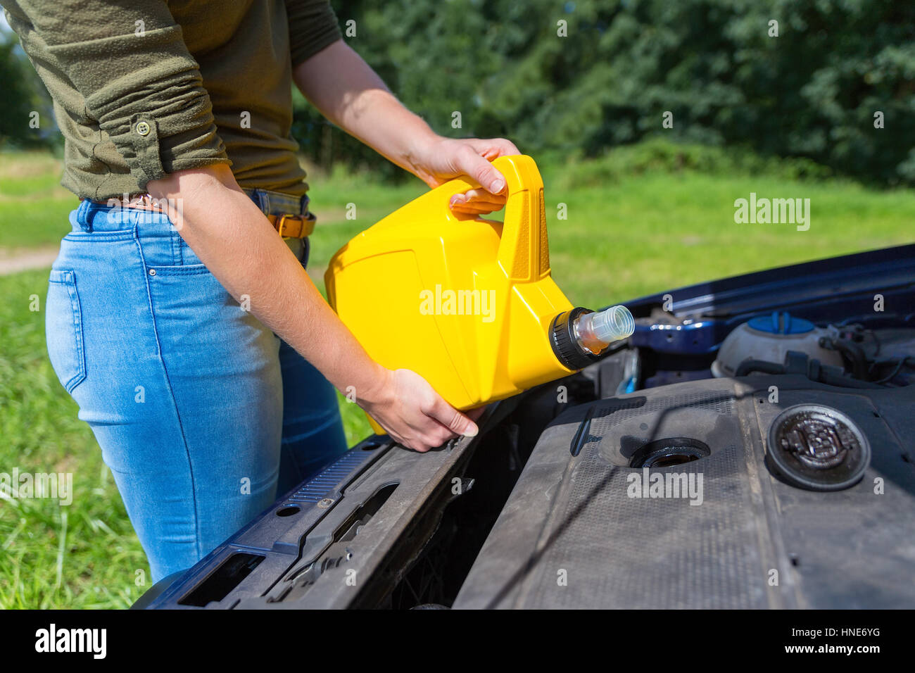 Young caucasian woman filling car motor with oil in yellow jerrycan Stock Photo