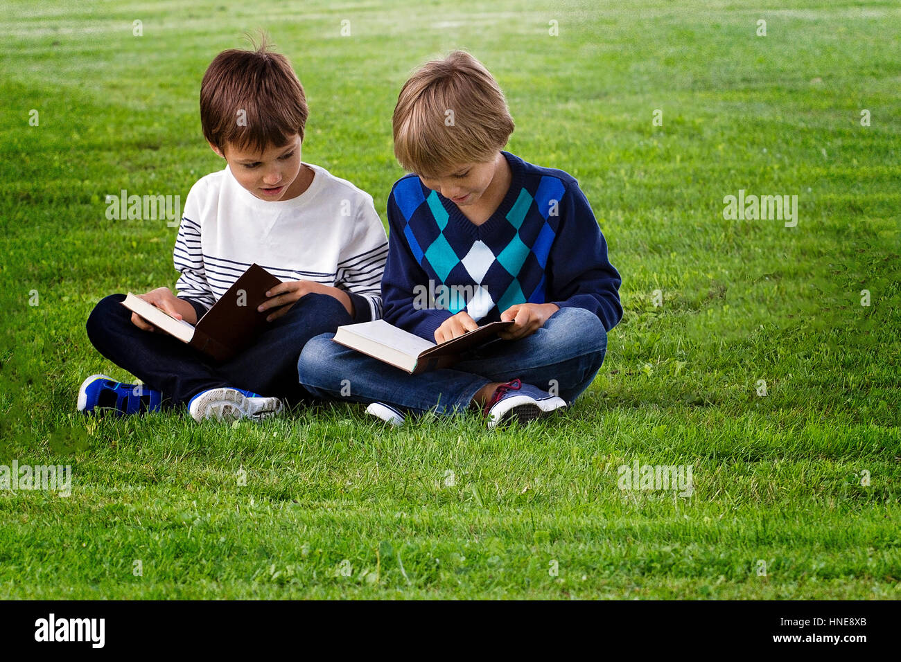 Little boys sitting on green grass in a park and reading books. Education, lifestyle, people concept Stock Photo