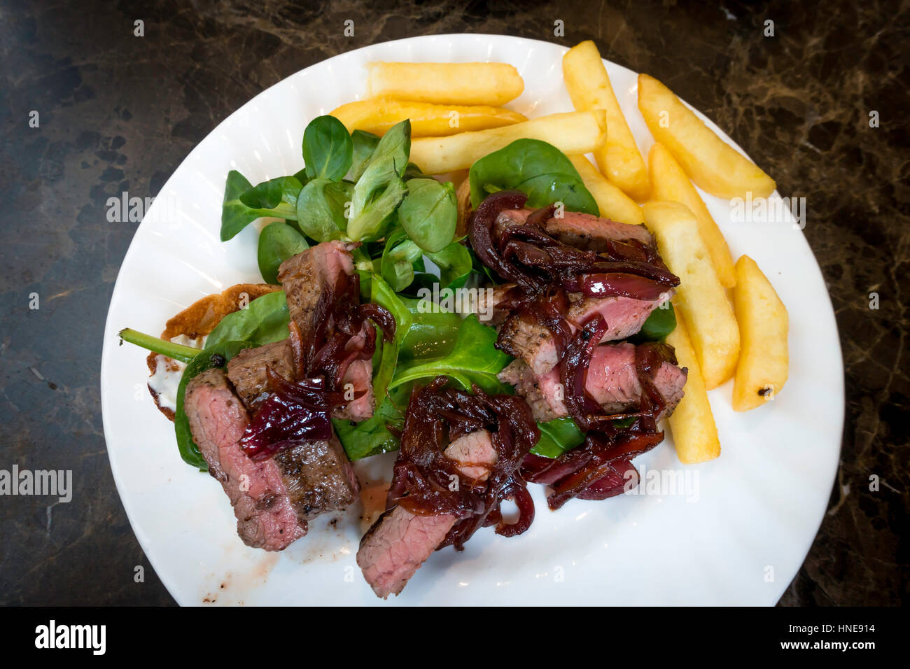 Lunchtime snack Steak open sandwich served with caramelised red onion, horseradish mayonnaise, baby leaf spinach and Chips Stock Photo