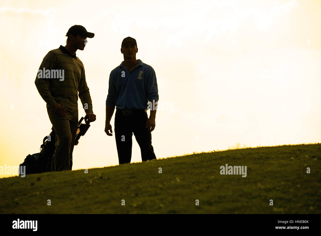 Silhouette of young men standing in golf course with trolley Stock Photo