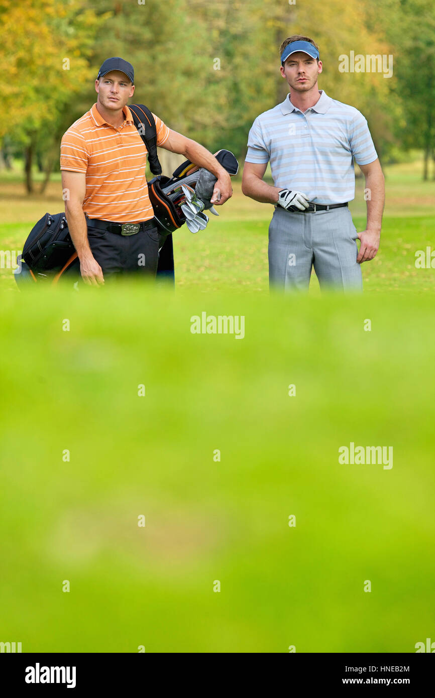 Young men standing on golf course carrying bags Stock Photo