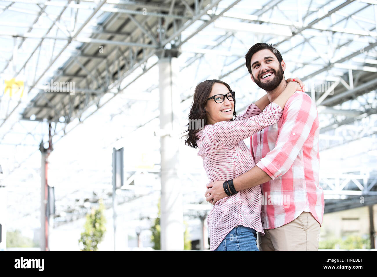 Happy couple looking away while embracing outside building Stock Photo