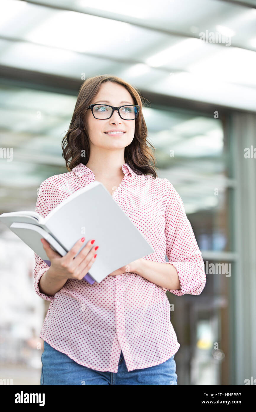 Thoughtful woman looking away while holding book outdoors Stock Photo