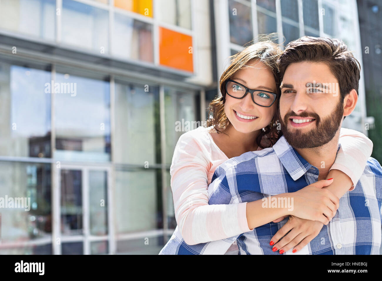 Loving man piggybacking woman in city Stock Photo