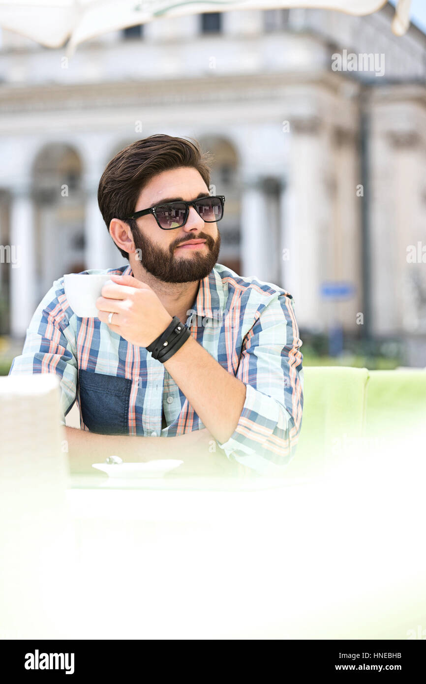Mid-adult man looking away while having coffee at sidewalk cafe Stock Photo