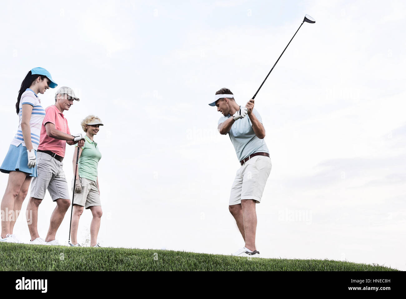 Friends looking at man playing golf against sky Stock Photo