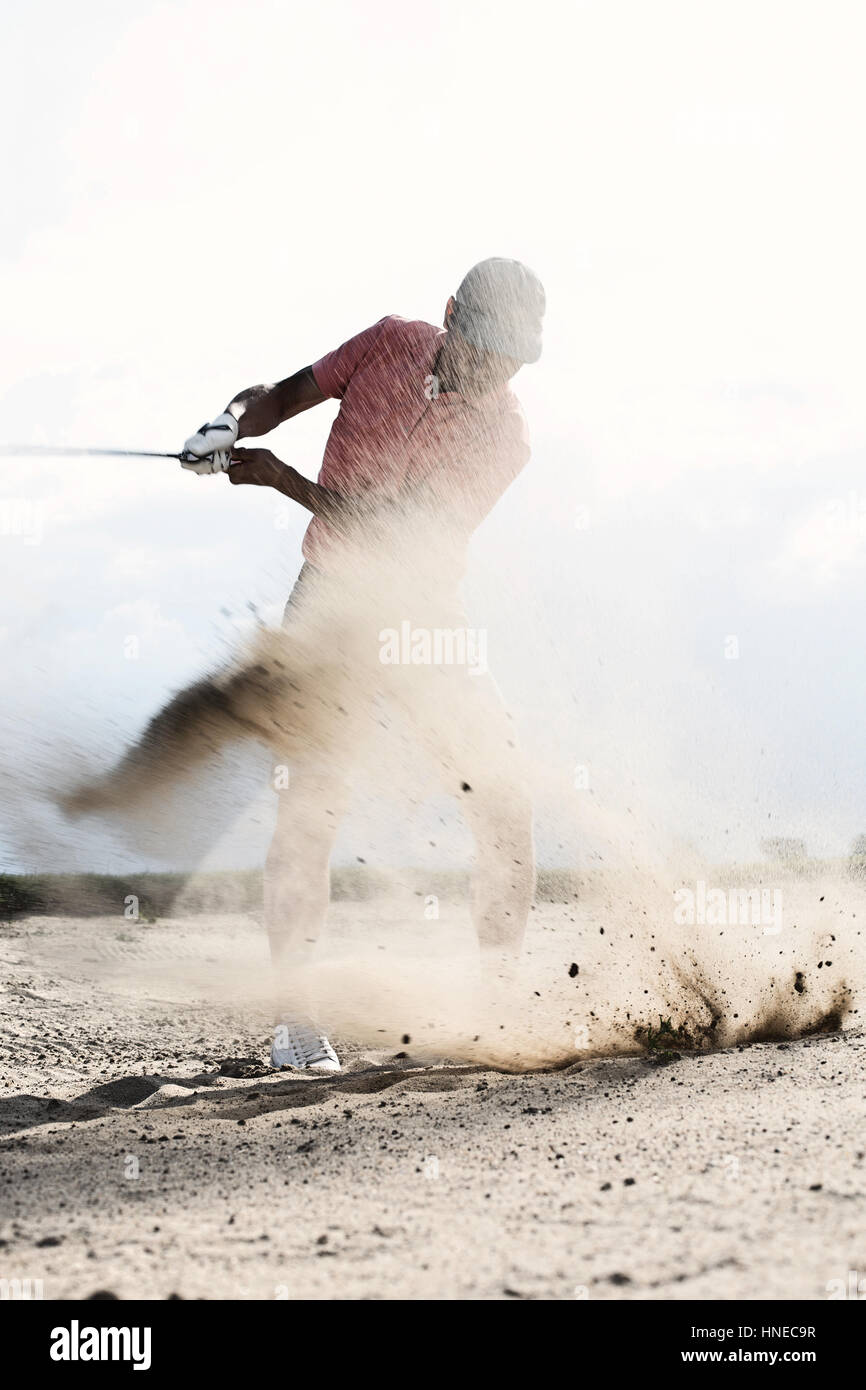 Middle-aged man splashing sand while playing at golf course Stock Photo