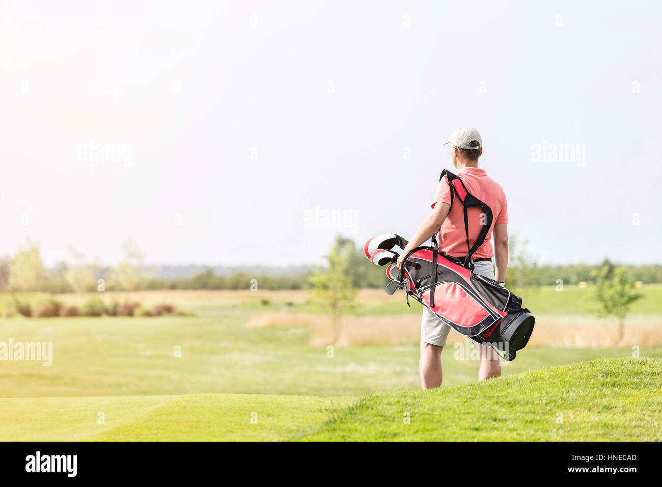 Rear view of man carrying golf club bag while walking at course Stock