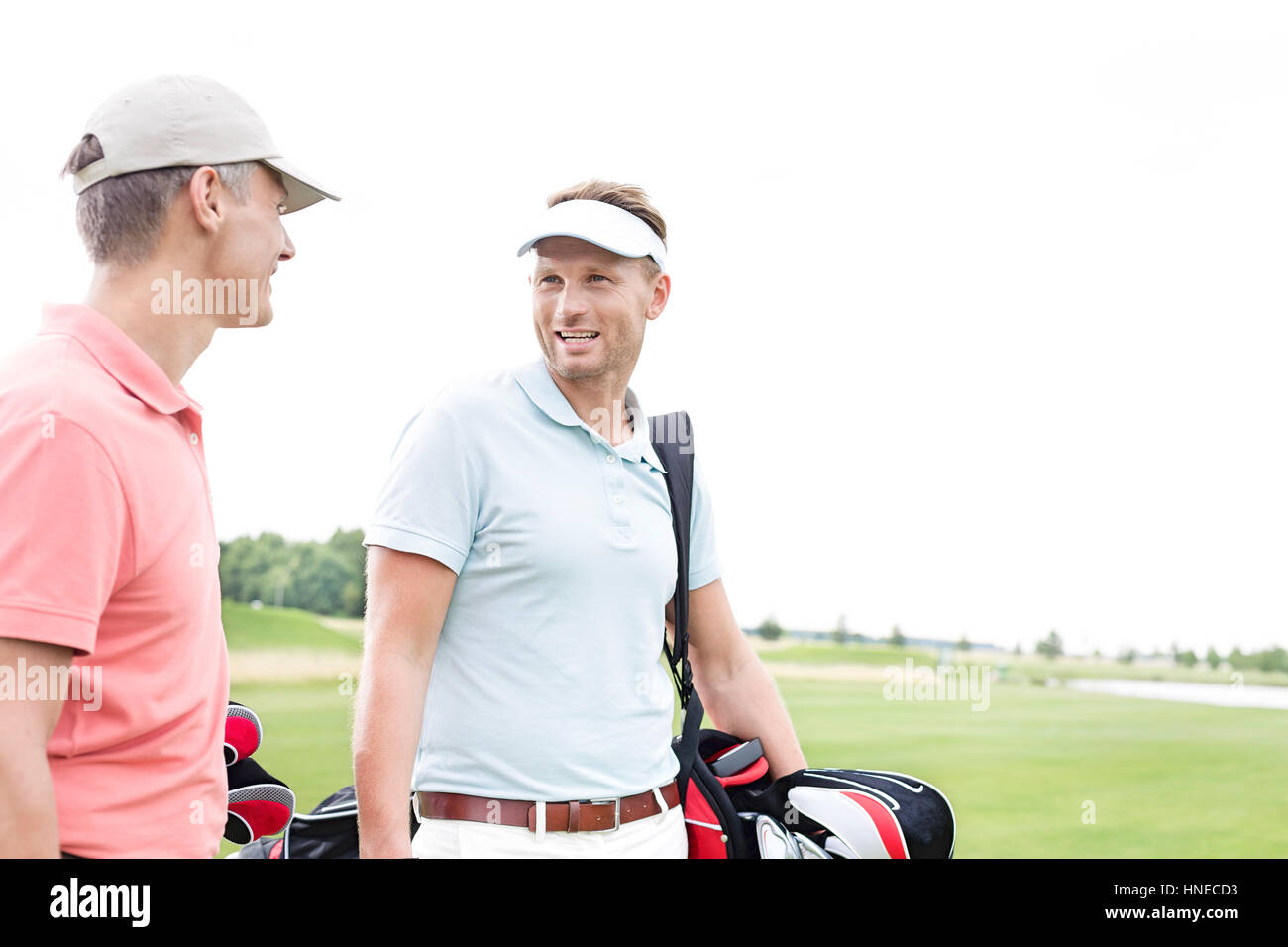 Happy golfer communicating with male friend against clear sky Stock Photo
