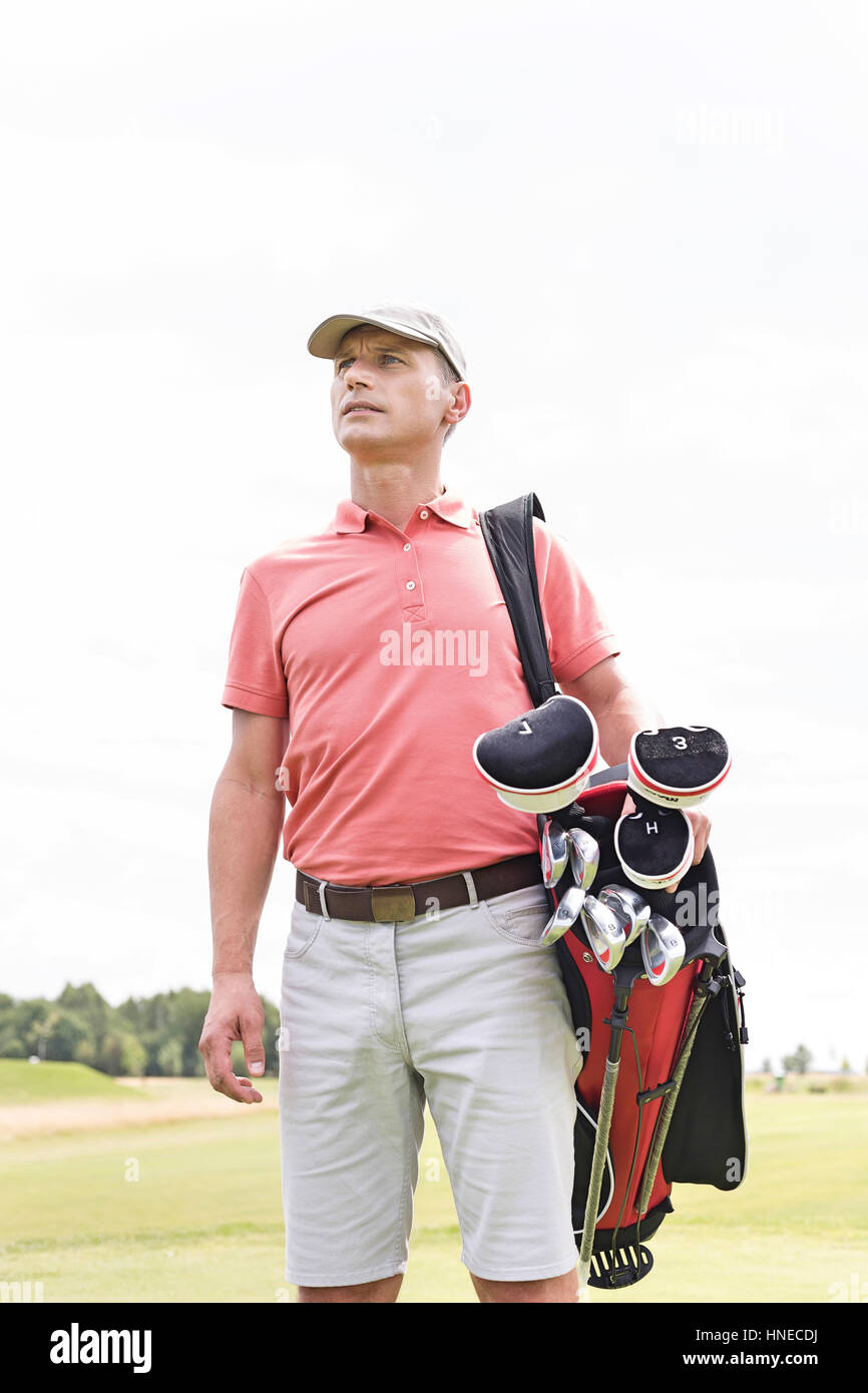 Thoughtful middle-aged man looking away while carrying golf bag against clear sky Stock Photo