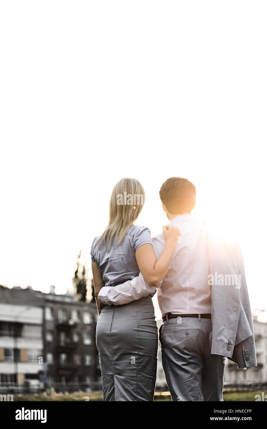 Rear view of business couple standing with arms around against clear sky on sunny day Stock Photo