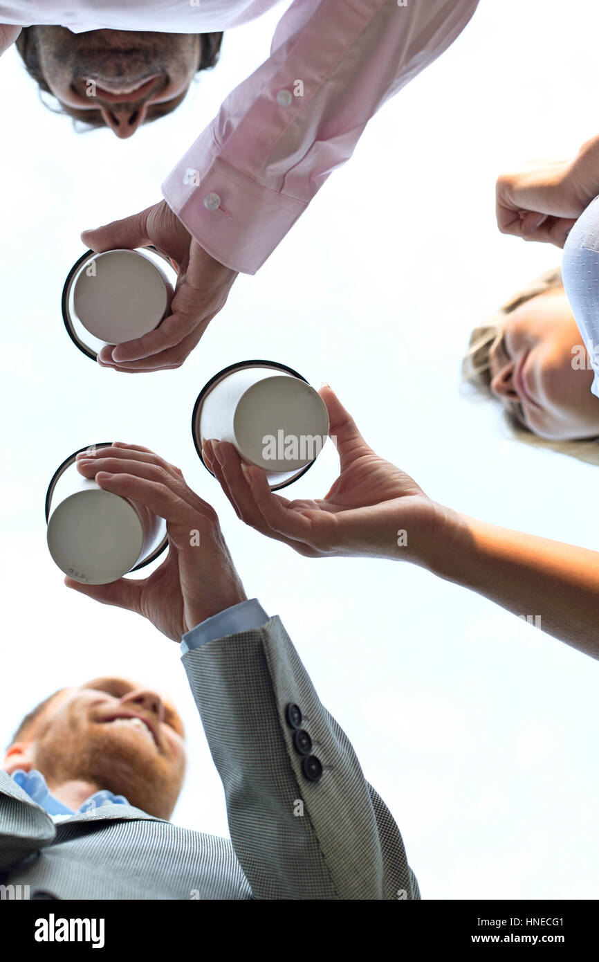 Directly below shot of businesspeople holding disposable cups against clear sky Stock Photo