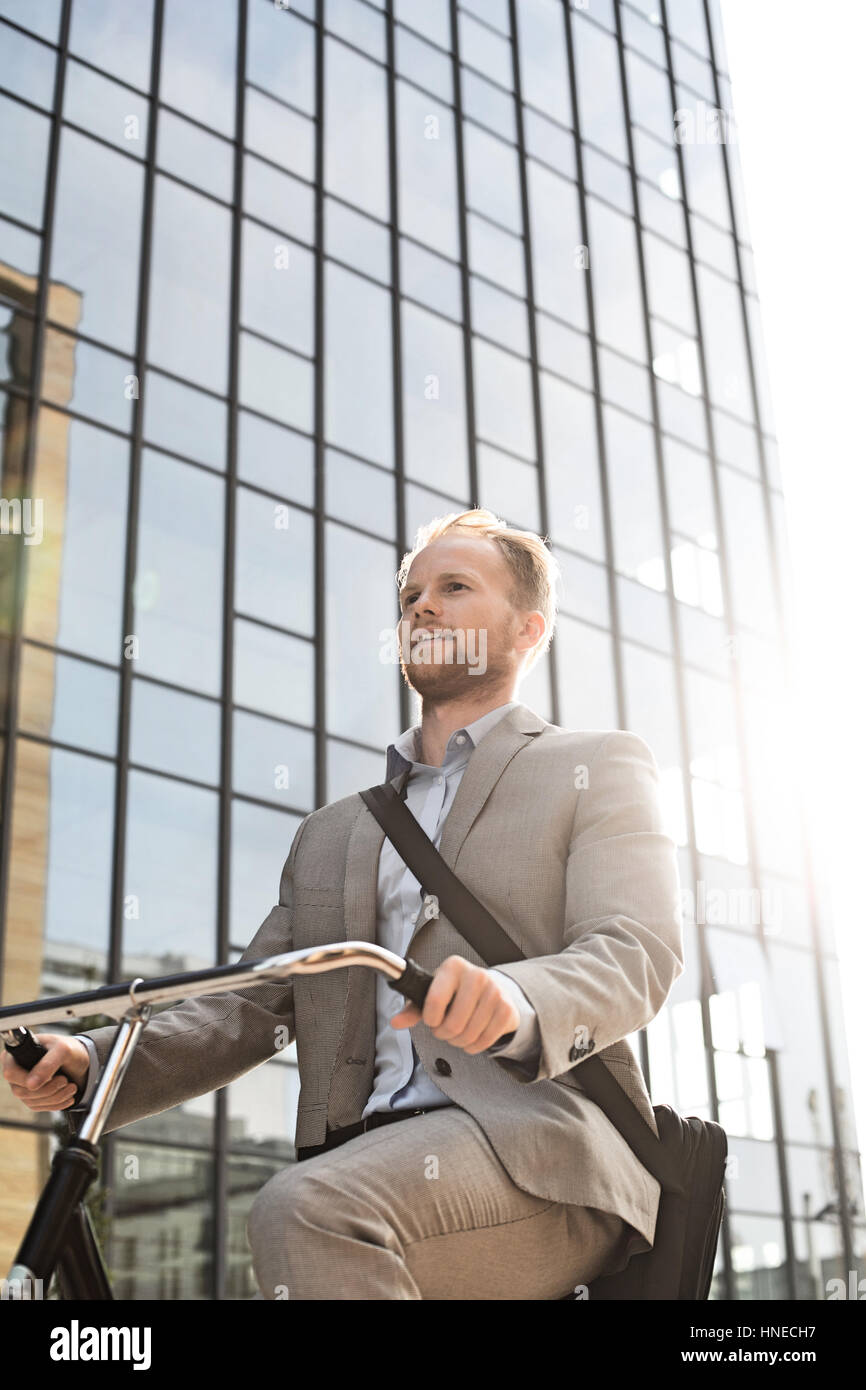 Low angle view of businessman riding bicycle outside office building on sunny day Stock Photo