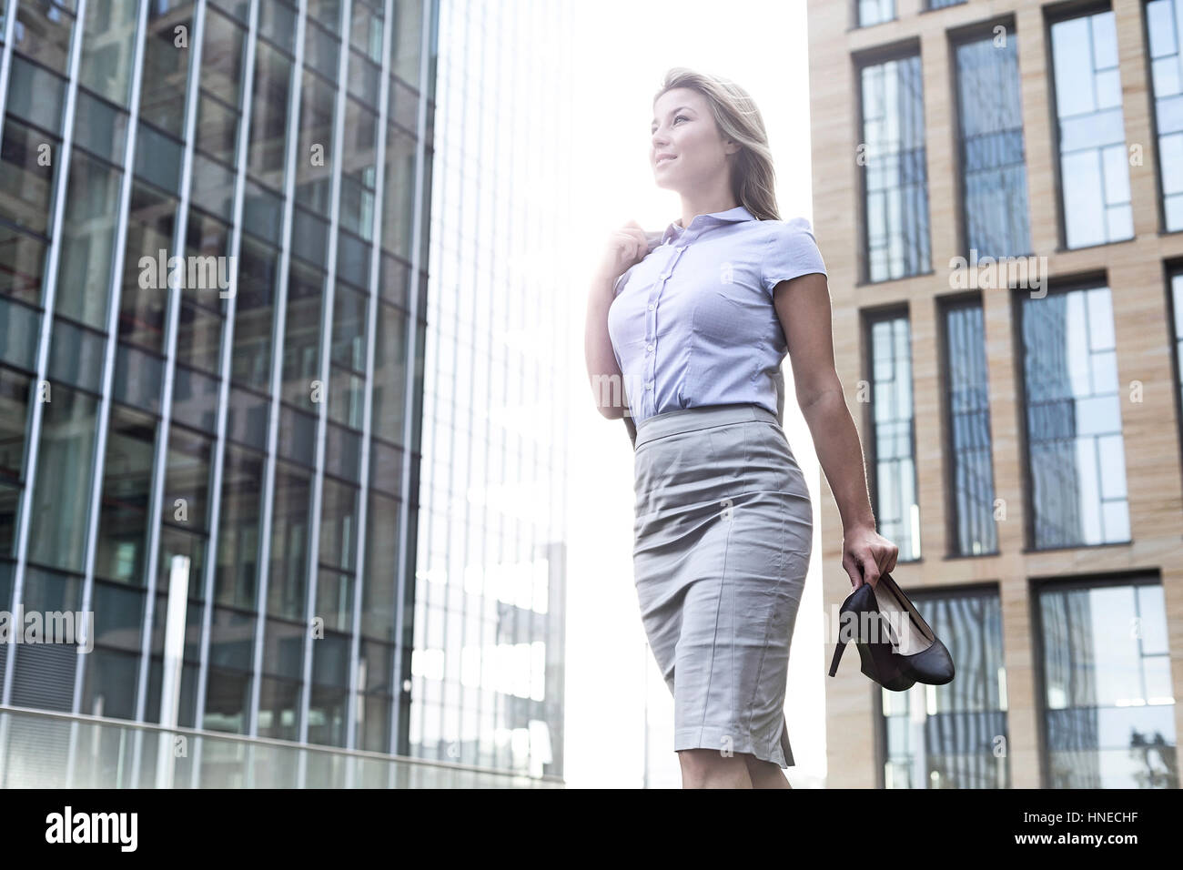 Low angle view of confident businesswoman holding high heels while standing outside office buildings Stock Photo