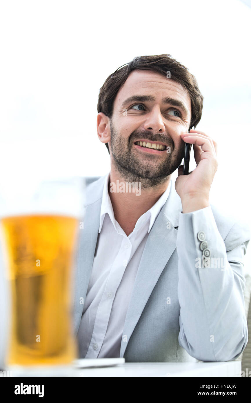 Happy businessman looking away while using mobile phone at outdoor restaurant Stock Photo