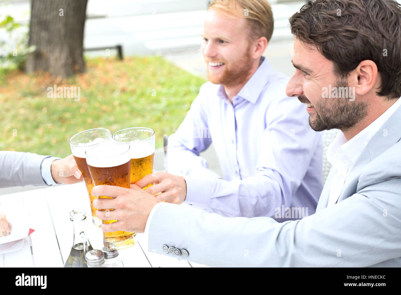 Businessmen toasting beer glasses with female colleague at outdoor restaurant Stock Photo
