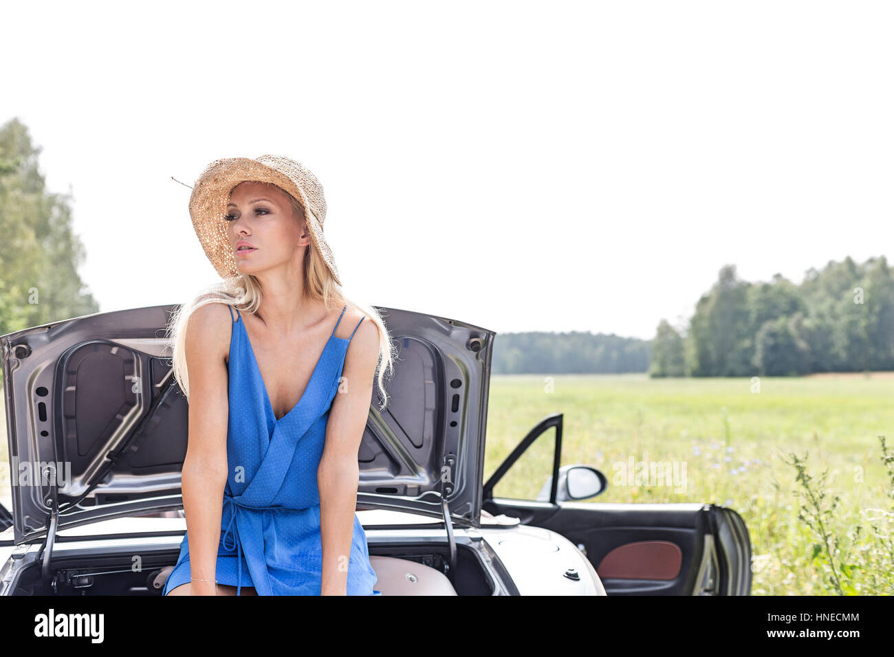 Woman looking away while sitting on convertible trunk against clear sky Stock Photo