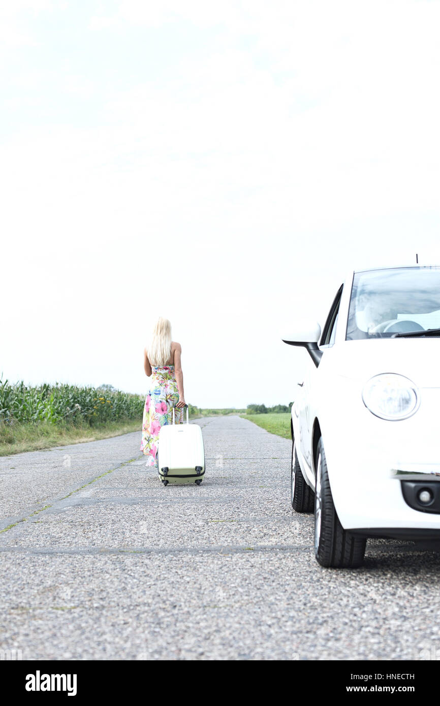 Rear view of woman with luggage leaving broken down car on country road Stock Photo