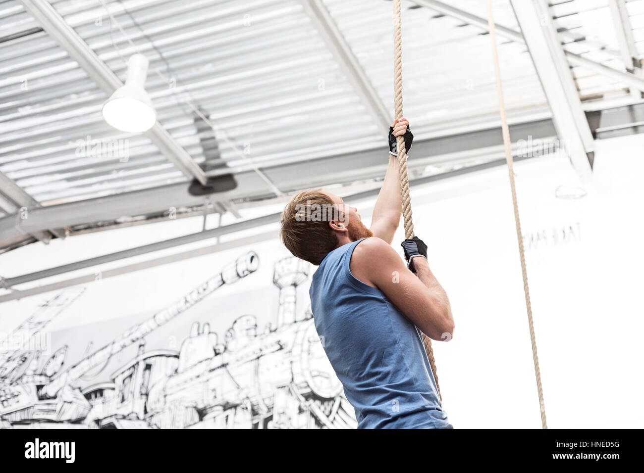 Side view of dedicated man climbing rope in crossfit gym Stock Photo
