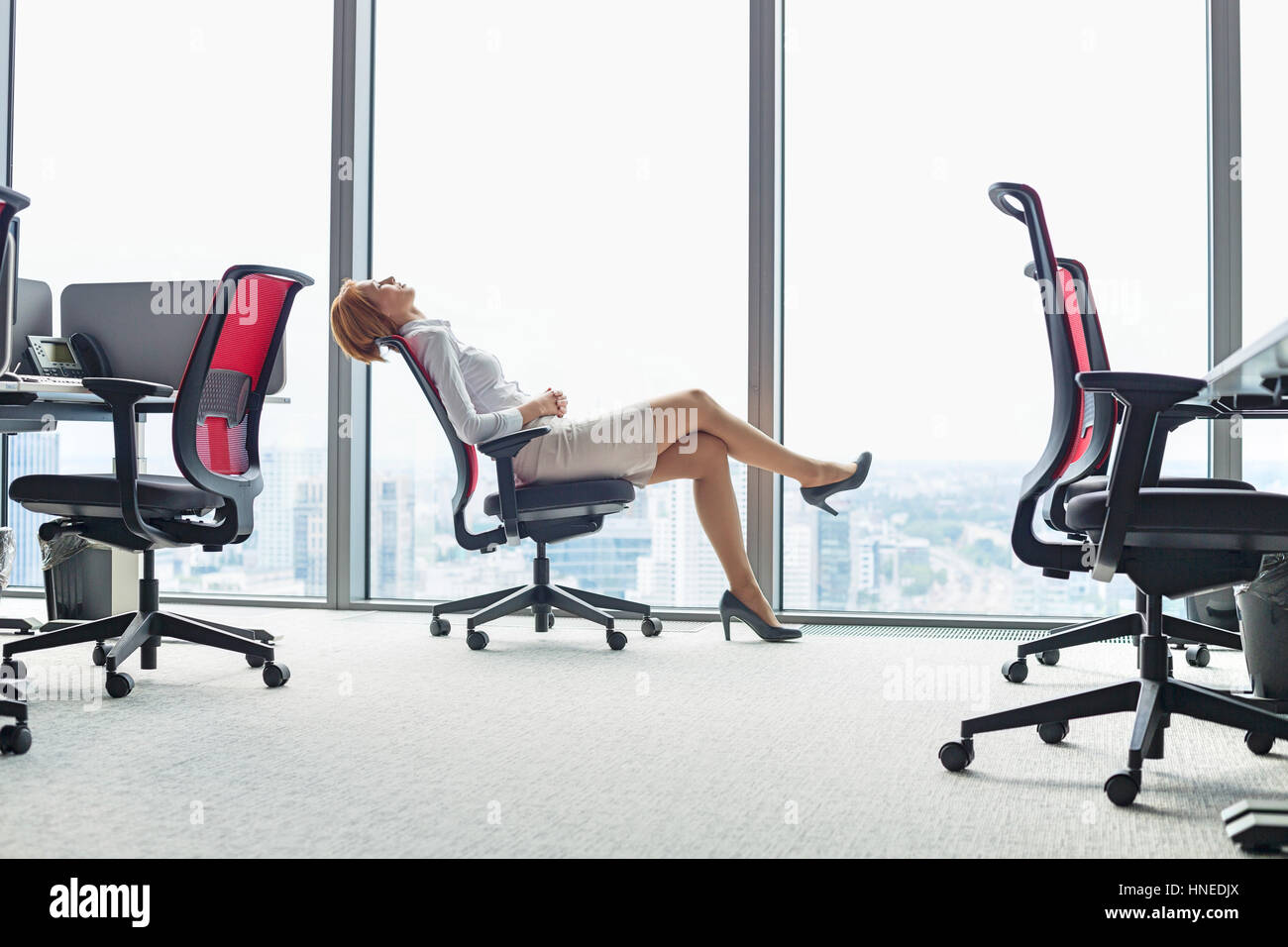 Full length side view of young businesswoman leaning back in chair at office  Stock Photo - Alamy