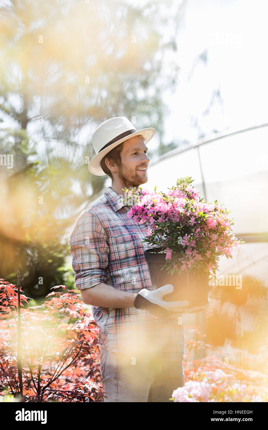 Smiling gardener looking away while holding flower pot outside greenhouse Stock Photo