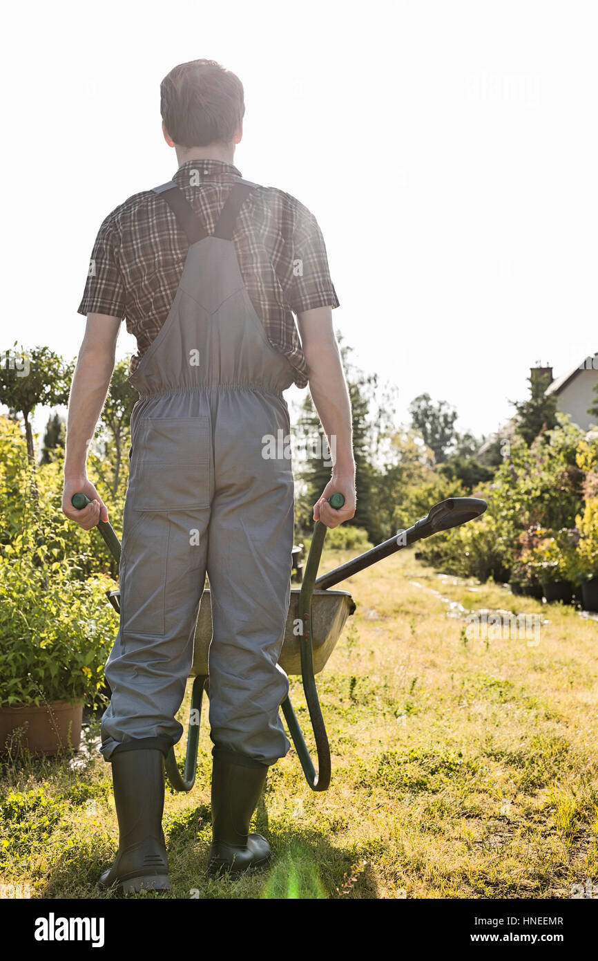 Full-length rear view of gardener pushing wheelbarrow at garden Stock Photo