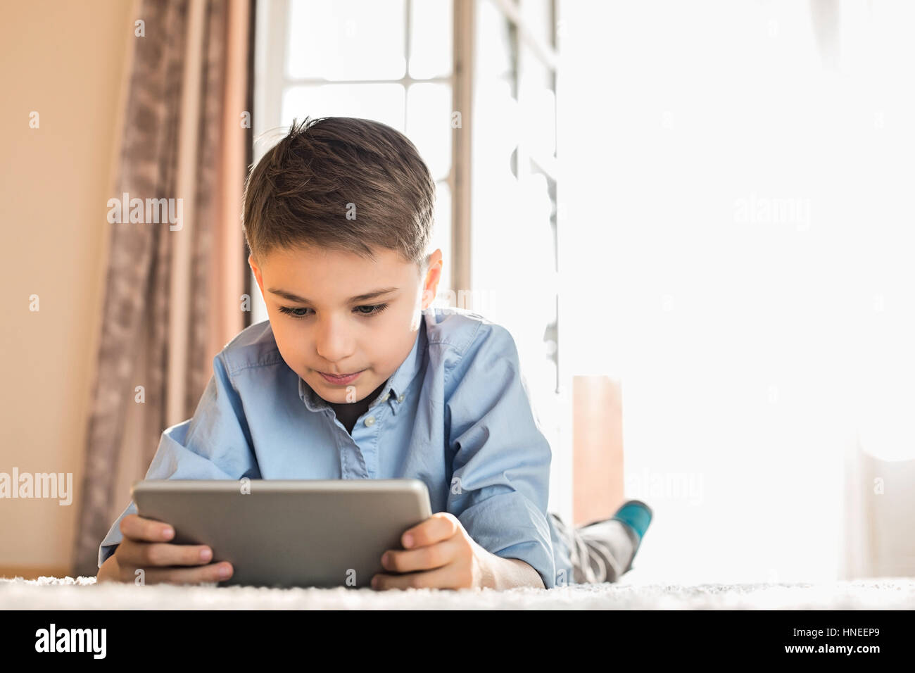 Boy using digital tablet while lying on floor at home Stock Photo - Alamy