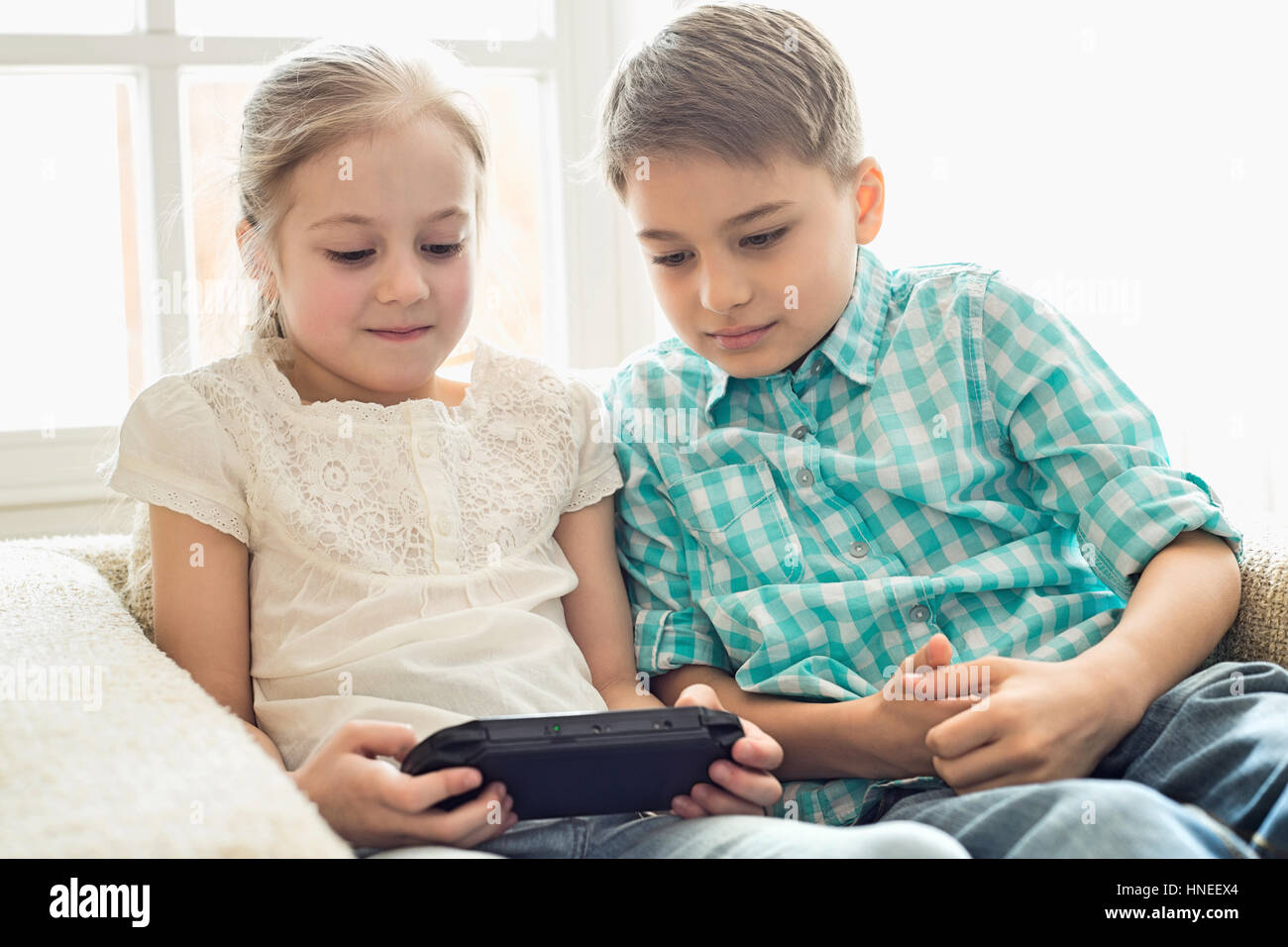 Siblings playing hand-held video game at home Stock Photo