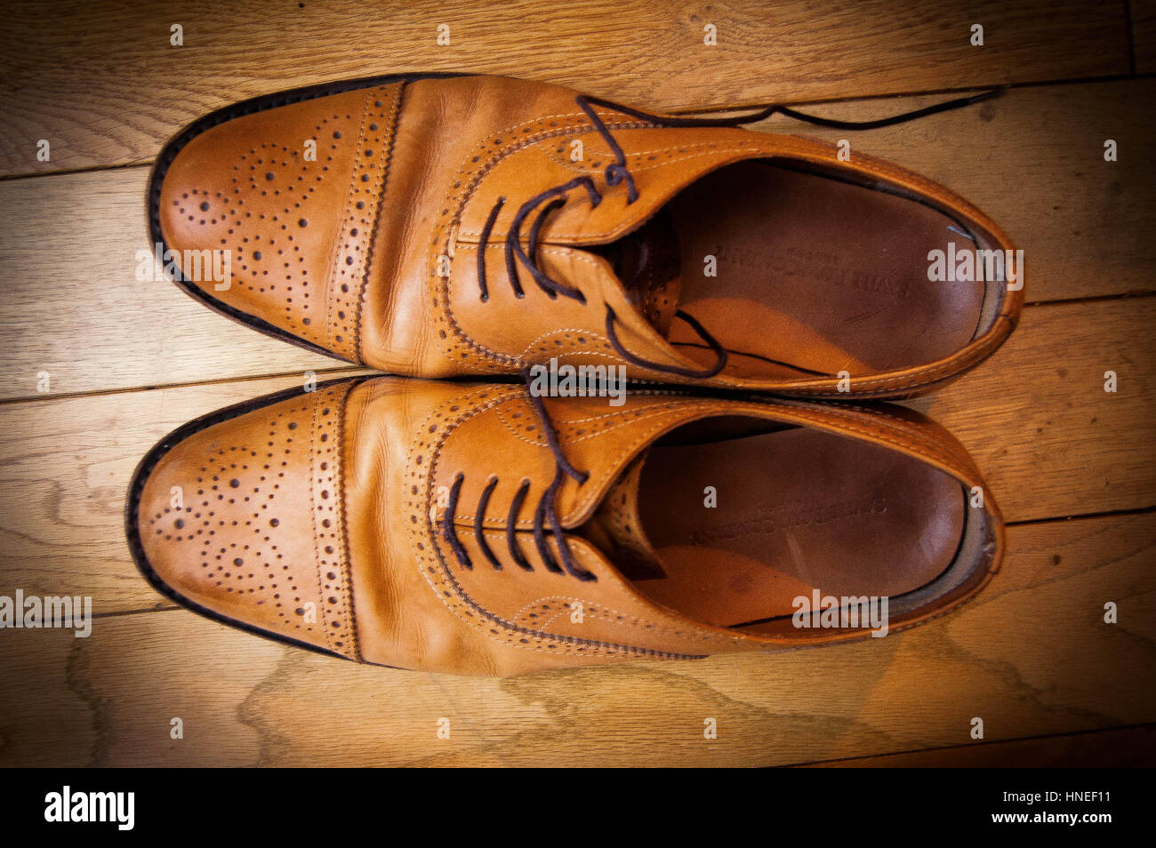 A pair of men's brown leather brogues on wooden flooring, shot from above, and one shoe toppled on its side. Stock Photo