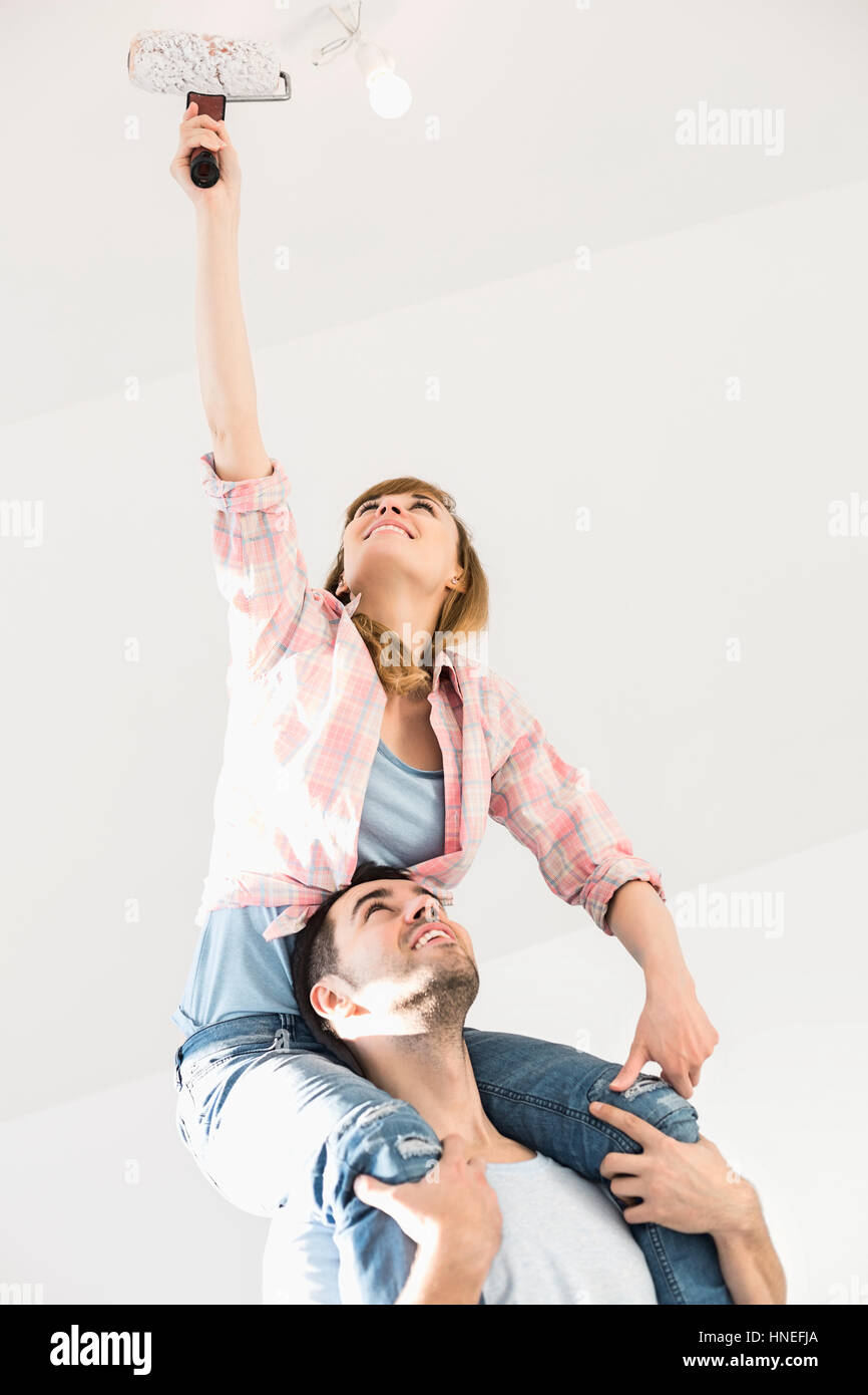 Woman on man's shoulders painting ceiling with paint roller Stock Photo