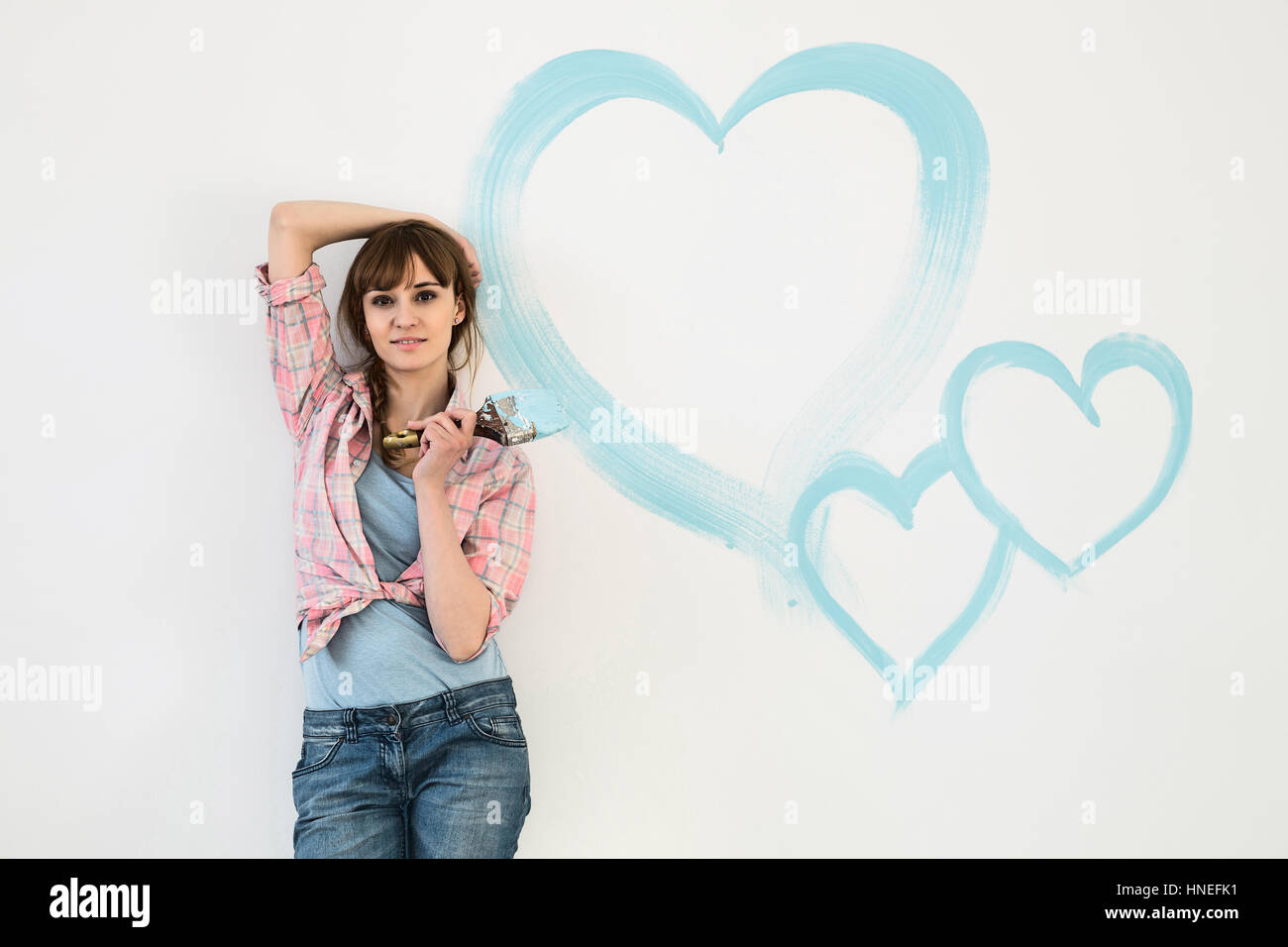 Portrait of beautiful woman holding paint brush with hearts painted on wall Stock Photo
