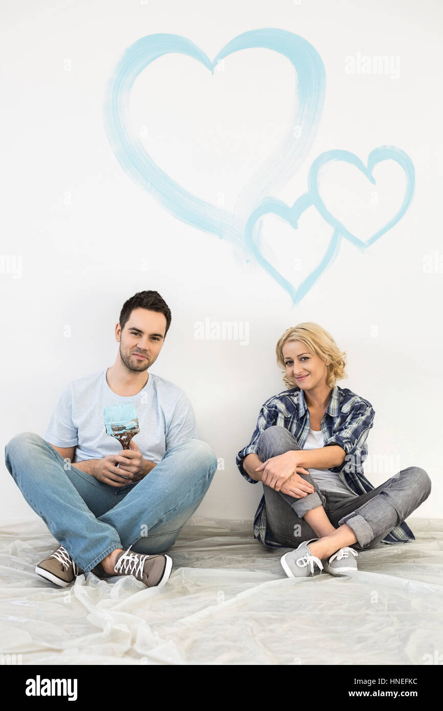 Full-length portrait of mid-adult couple with painted hearts on wall Stock Photo