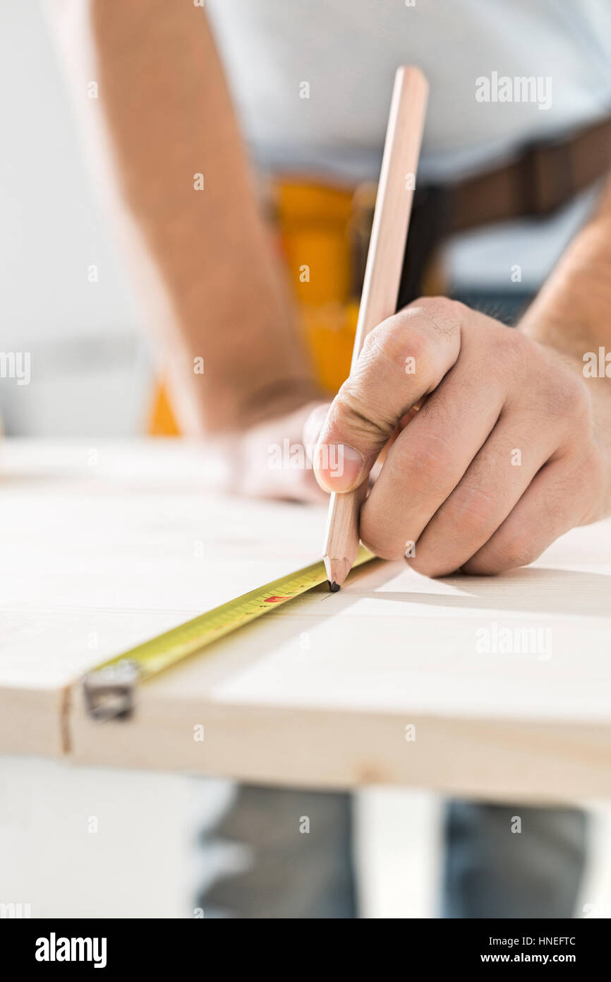 Midsection of carpenter marking table with measure tape Stock Photo