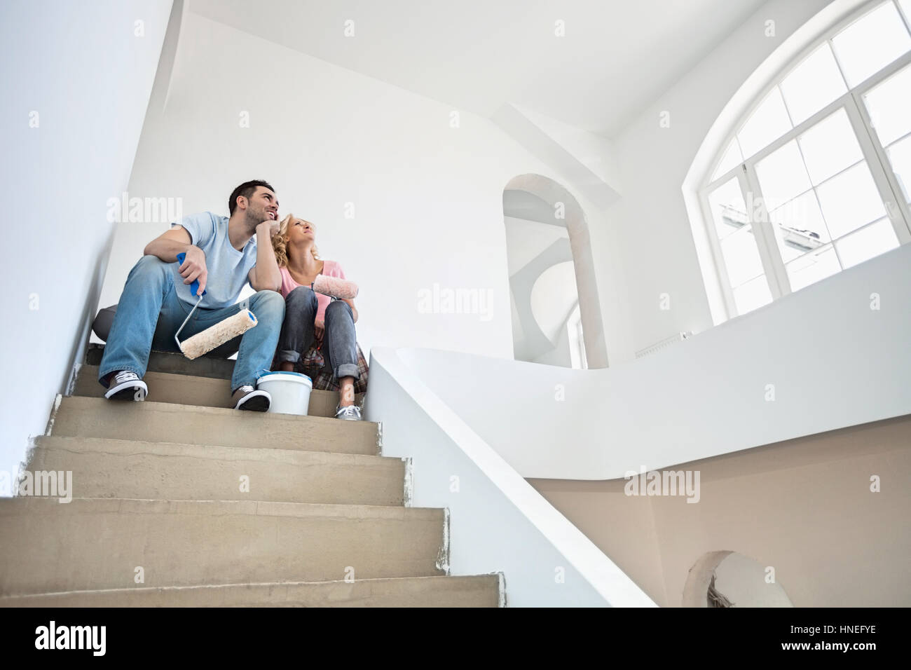Low angle view of couple with painting tools sitting on steps in new house Stock Photo