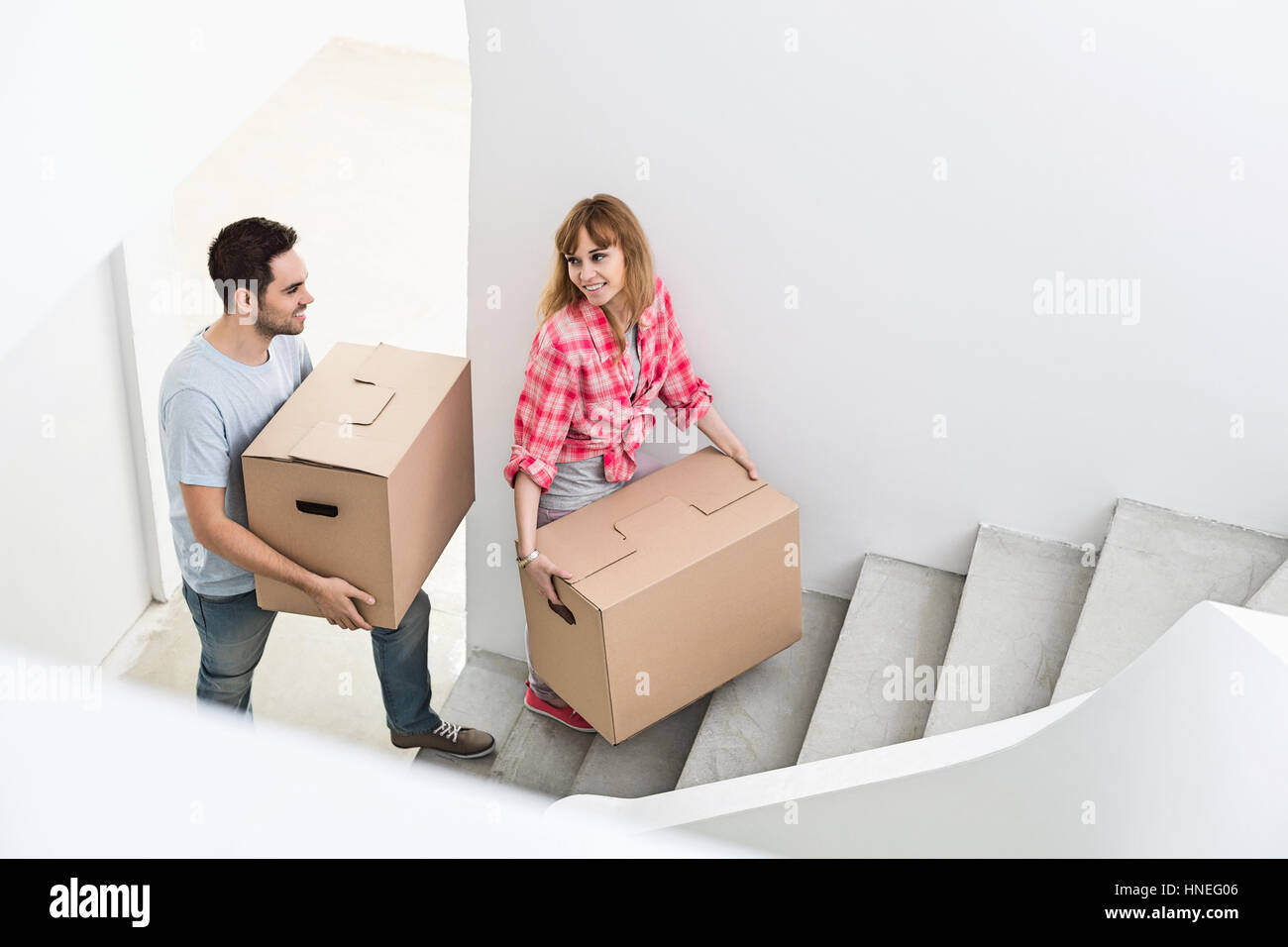 Happy couple carrying moving boxes up stairs in new house Stock Photo