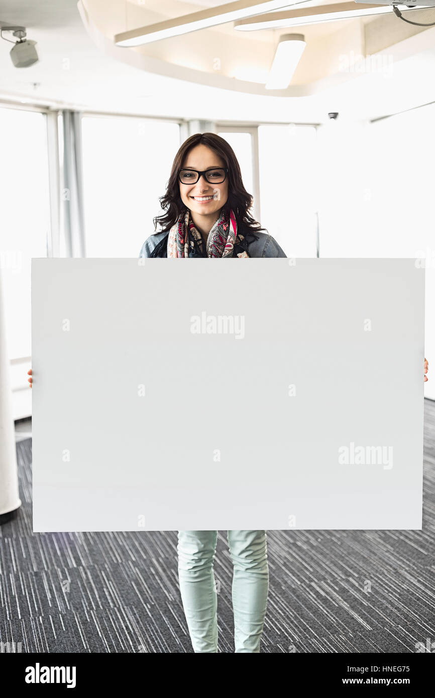 Portrait of happy businesswoman holding blank sign in creative office Stock Photo