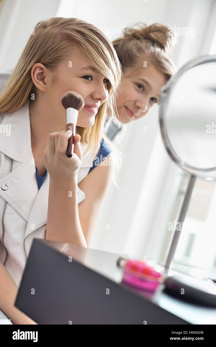 Girl watching sister applying makeup in front of mirror at home Stock Photo