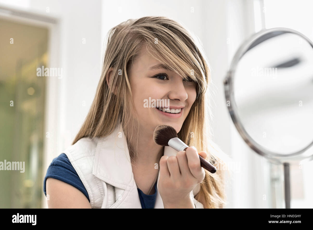 Girl applying makeup in front of mirror at home Stock Photo
