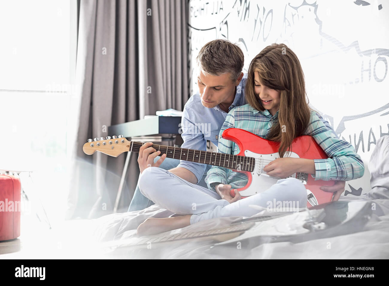 Father teaching daughter to play electric guitar at home Stock Photo