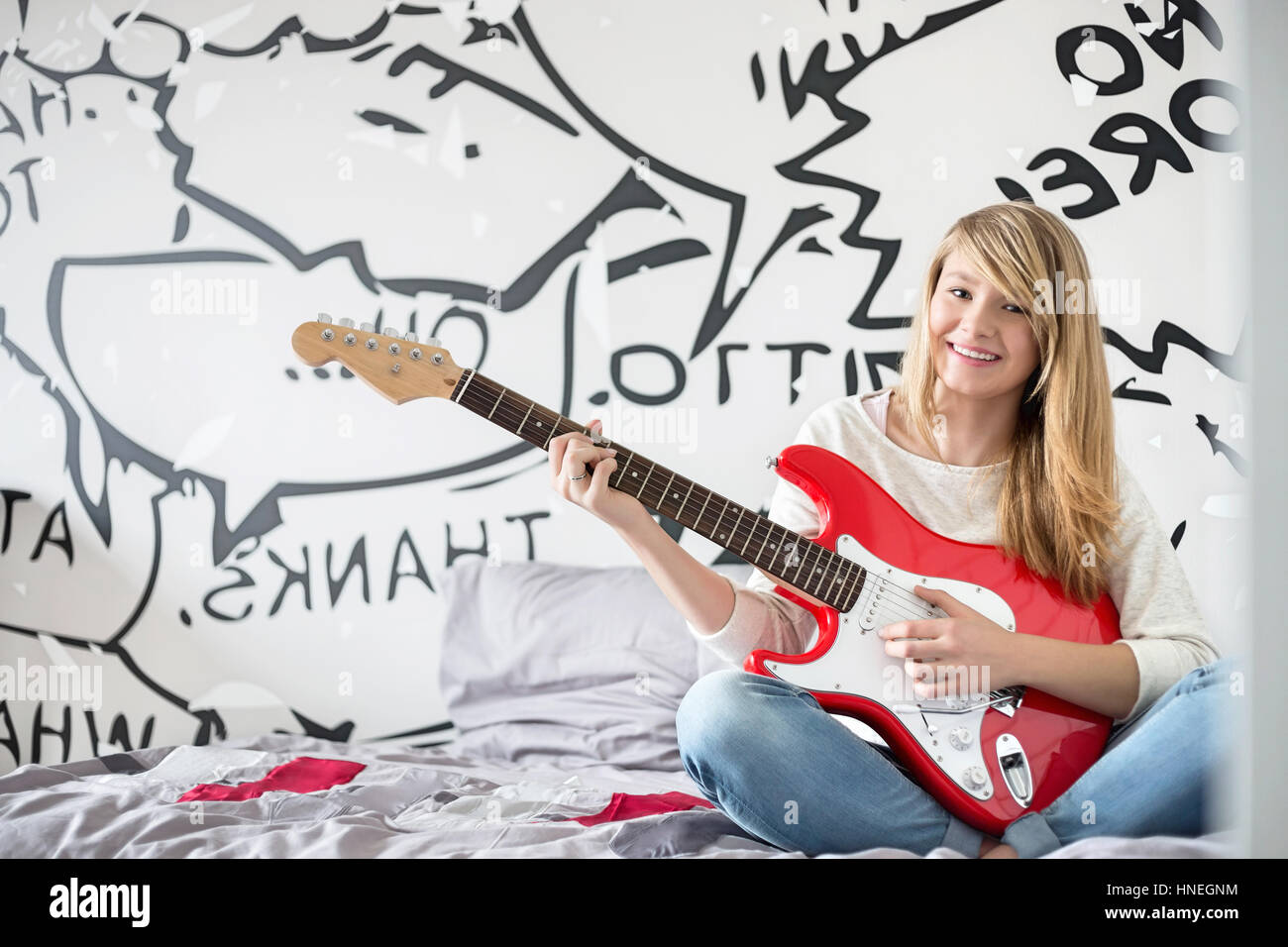 Fulllength portrait of teenage girl playing guitar in bedroom Stock