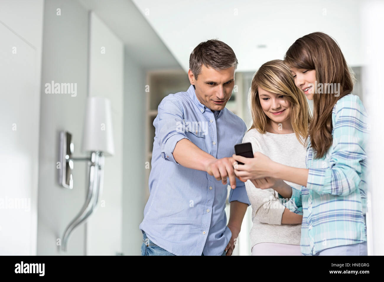 Middle-aged man with daughters using smart phone at home Stock Photo