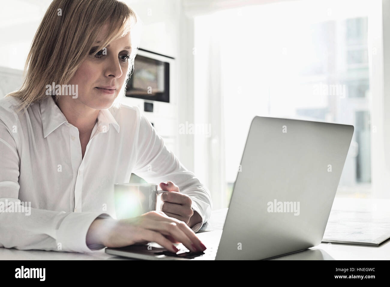 Beautiful mid adult businesswoman using laptop while having coffee at home Stock Photo