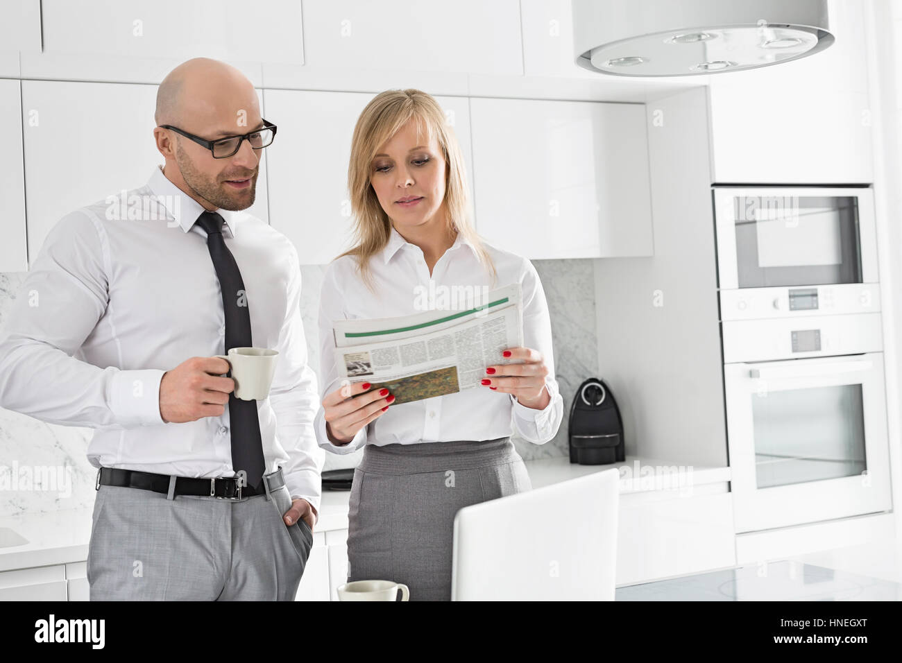 Mid adult business couple reading newspaper while having coffee in kitchen Stock Photo