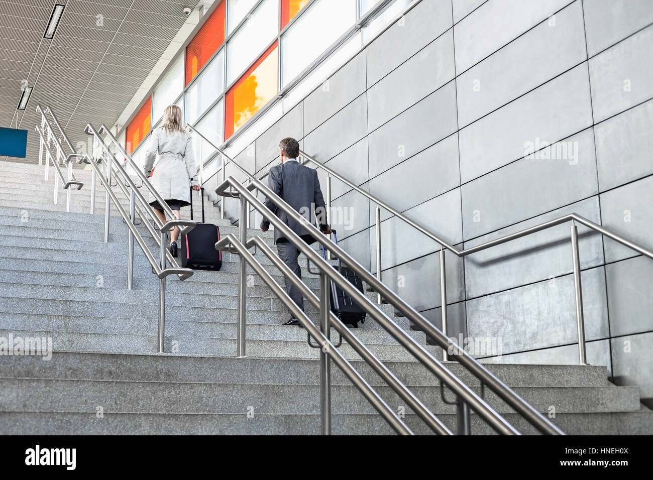 Rear view of businessman and businesswoman with luggage moving upstairs in railroad station Stock Photo